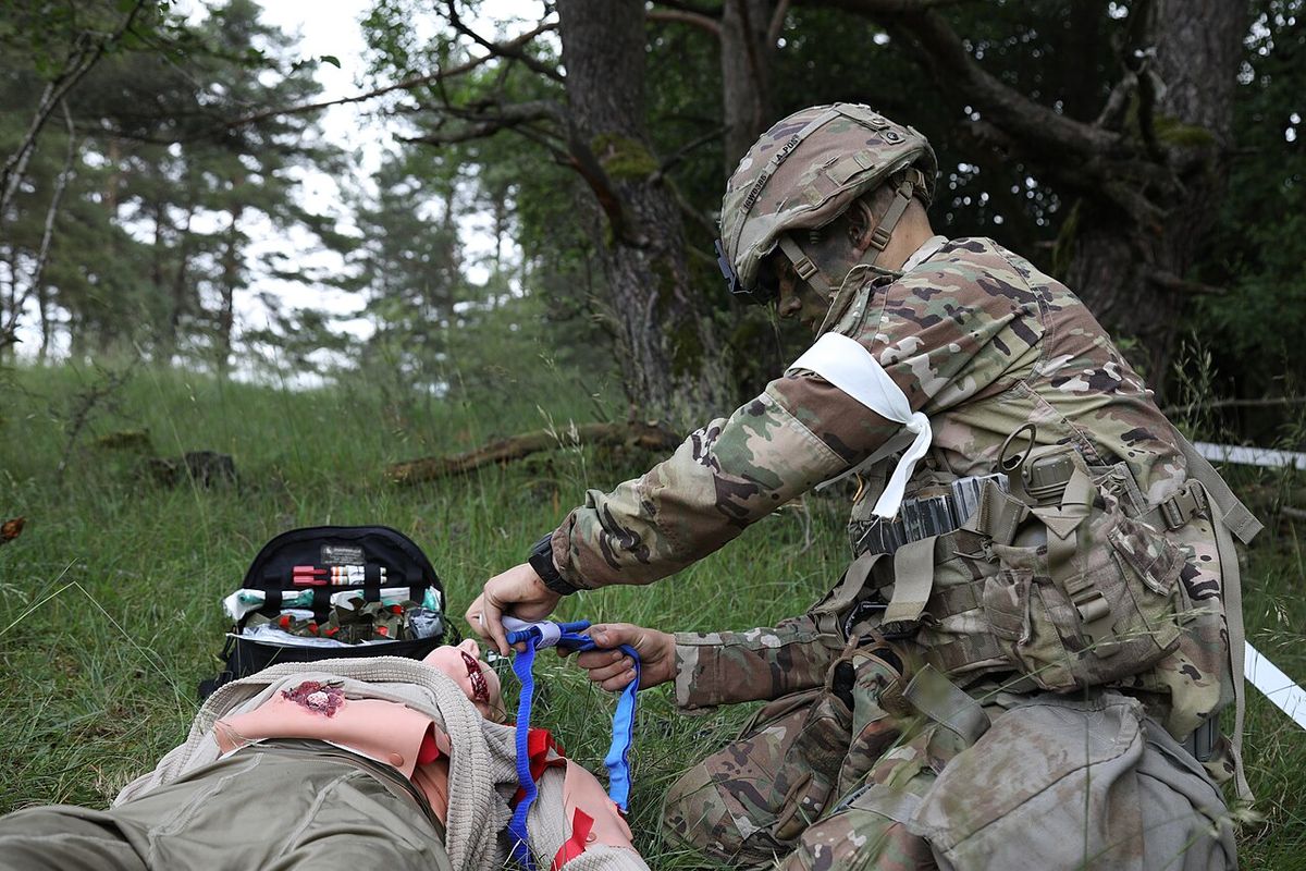 A soldier tightening a tourniquet band on a training dummy's leg