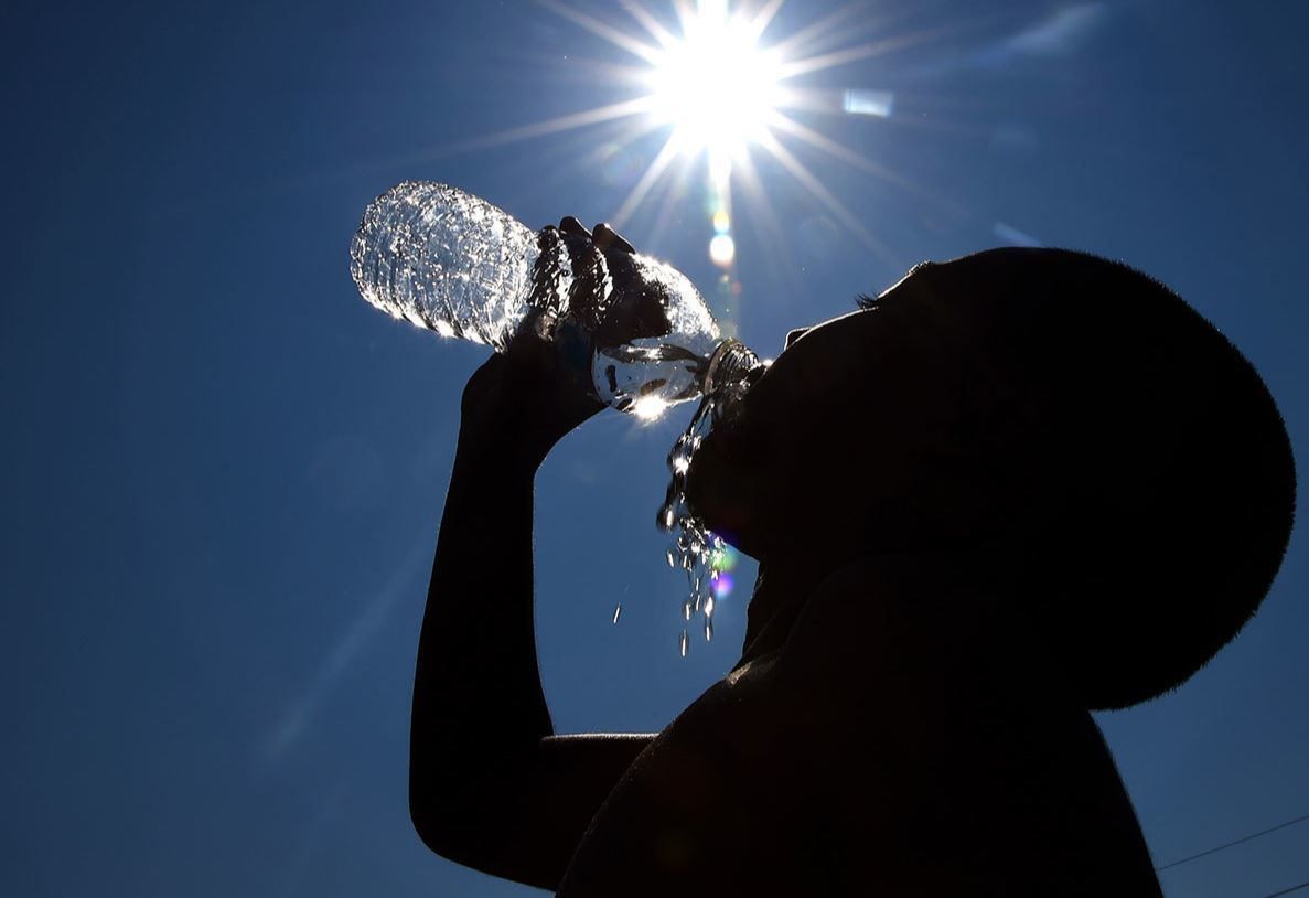 A silhouetted person drinking from a water bottle under a blazing sun