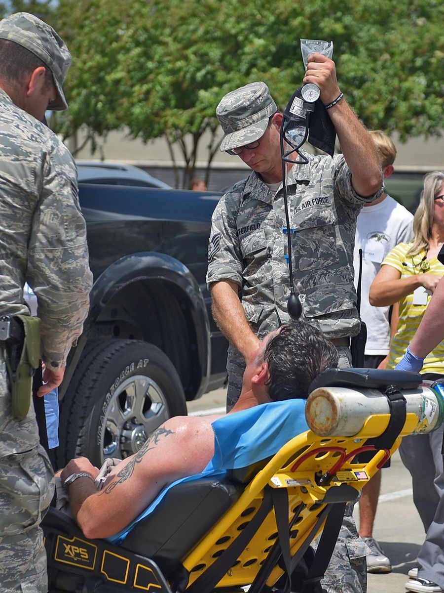 Medics pouring water over a soldier lying on a stretcher in the shade