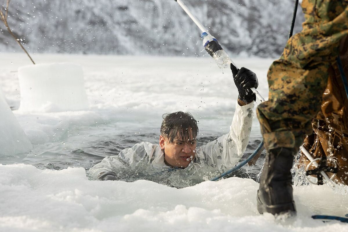 A man chest-deep in a hole cut in lake ice, being pulled out by rope