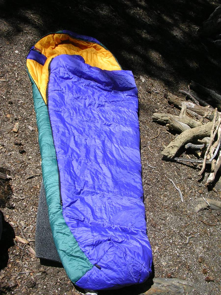 A blue mummy-style sleeping bag laid out on the ground