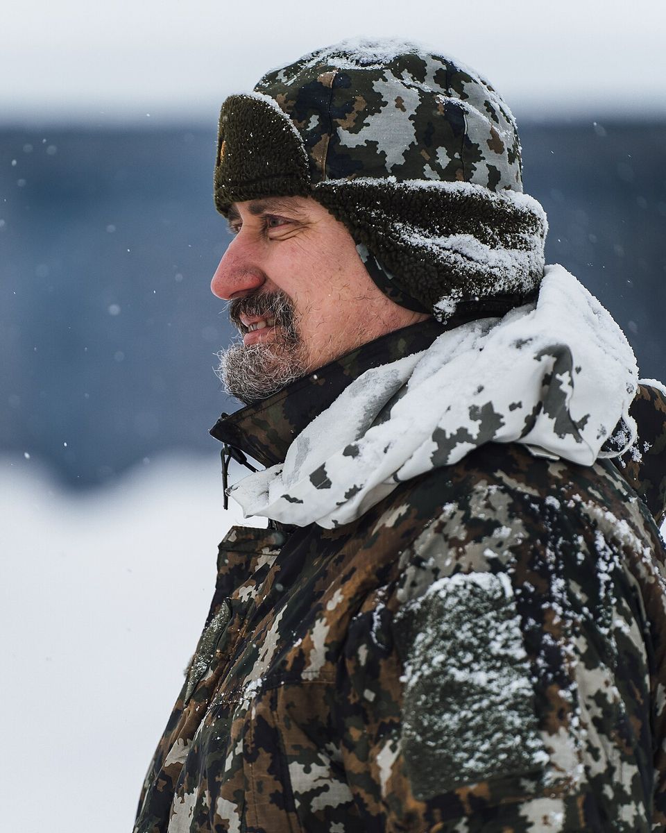 A man in a fur-lined hat with ear flaps and a hood in falling snow