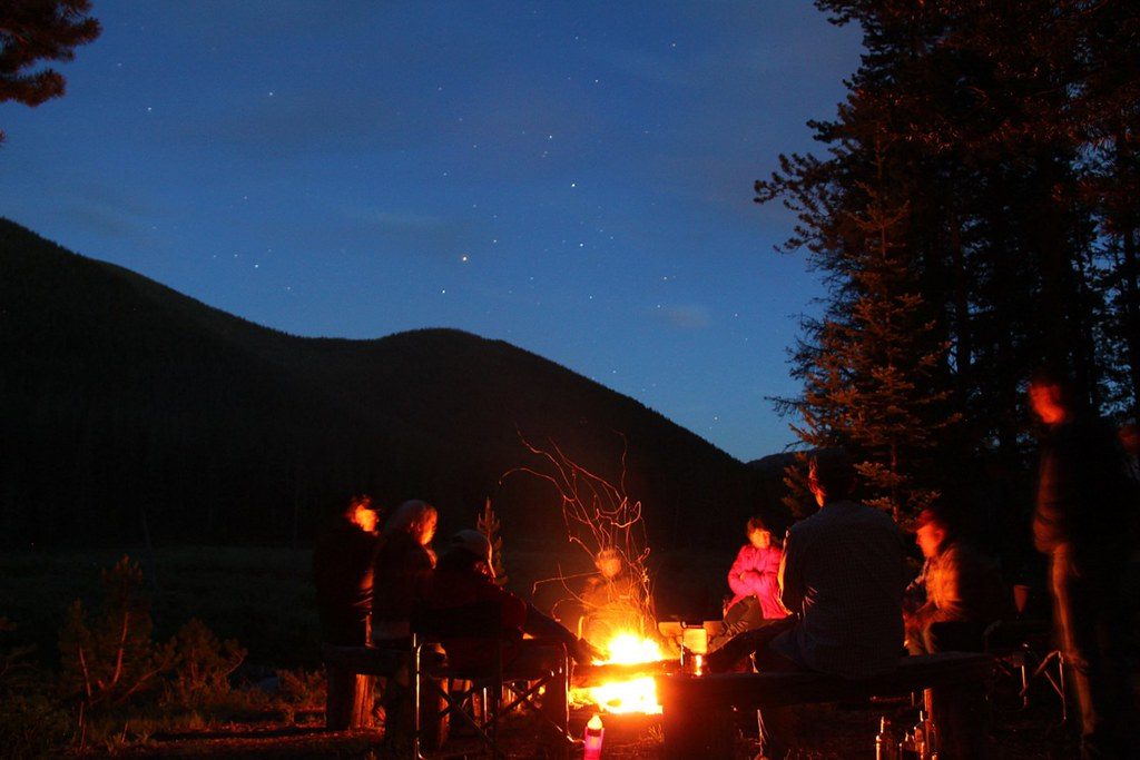 People around a small campfire at dusk below a mountain