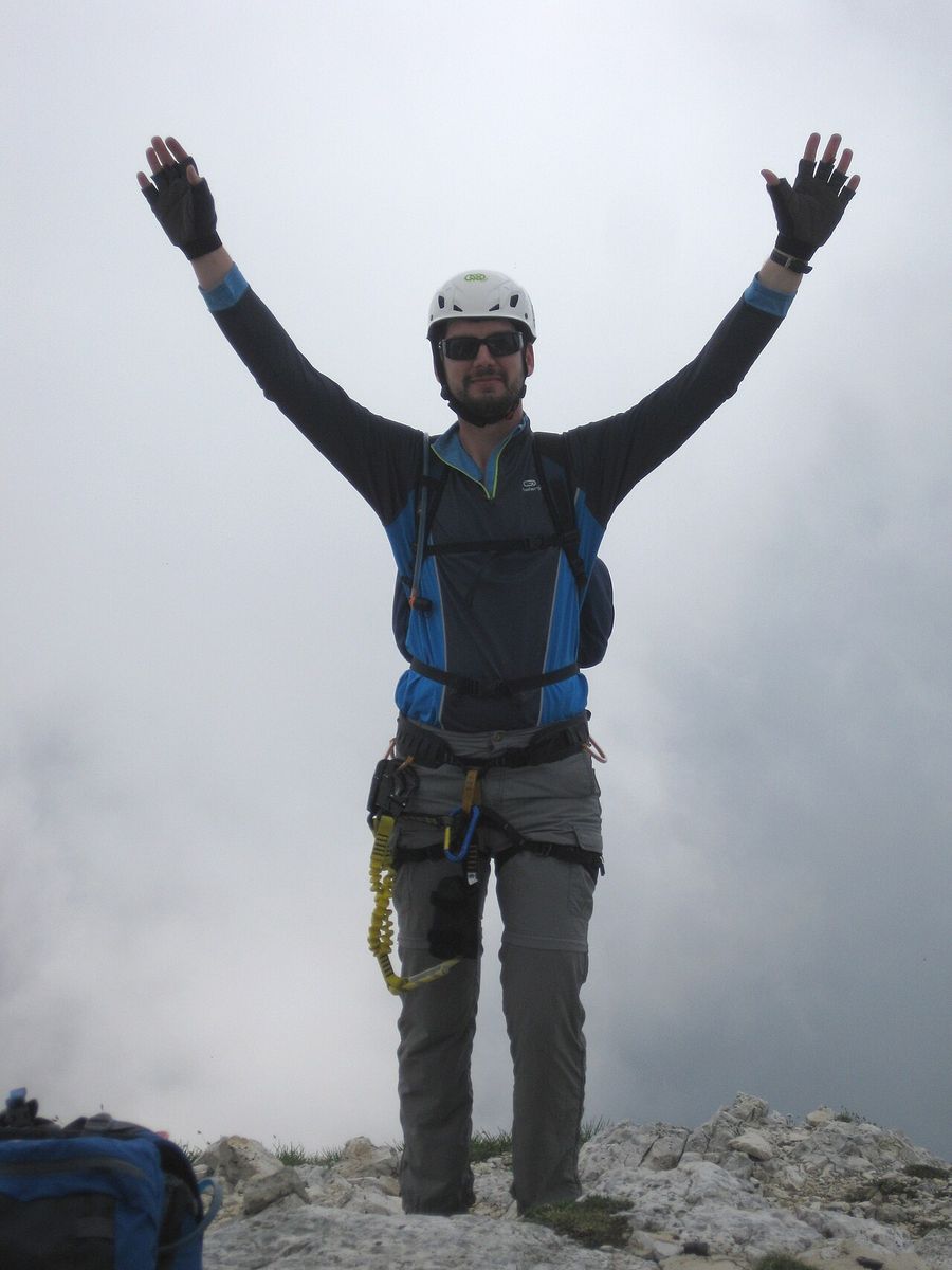 A hiker standing on a summit with both arms raised straight up