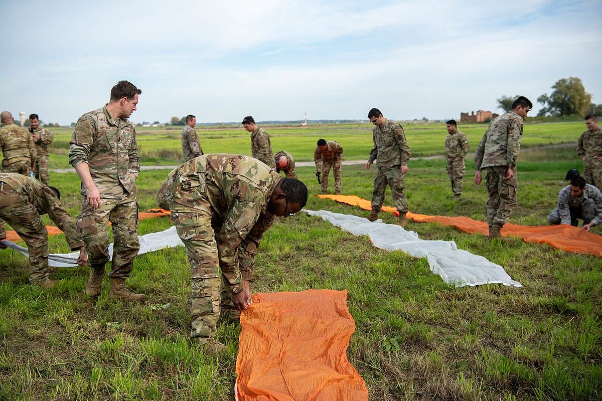 Soldiers laying out large orange and white panels in a geometric pattern on a field