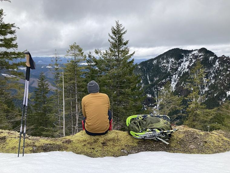 A hiker seen from behind, sitting still on a ridge with pack set down