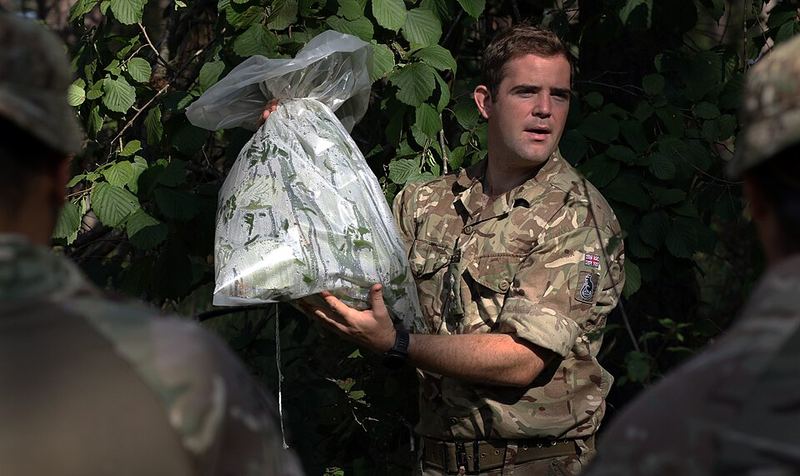 A soldier holds up a clear plastic bag tied over leafy branches with water inside