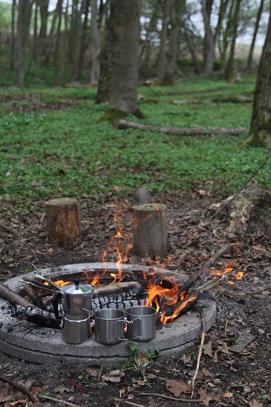 Metal pots and a kettle heating over a campfire in a stone ring