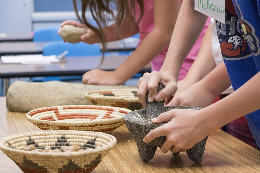 Hands grinding acorns with a stone mortar and pestle