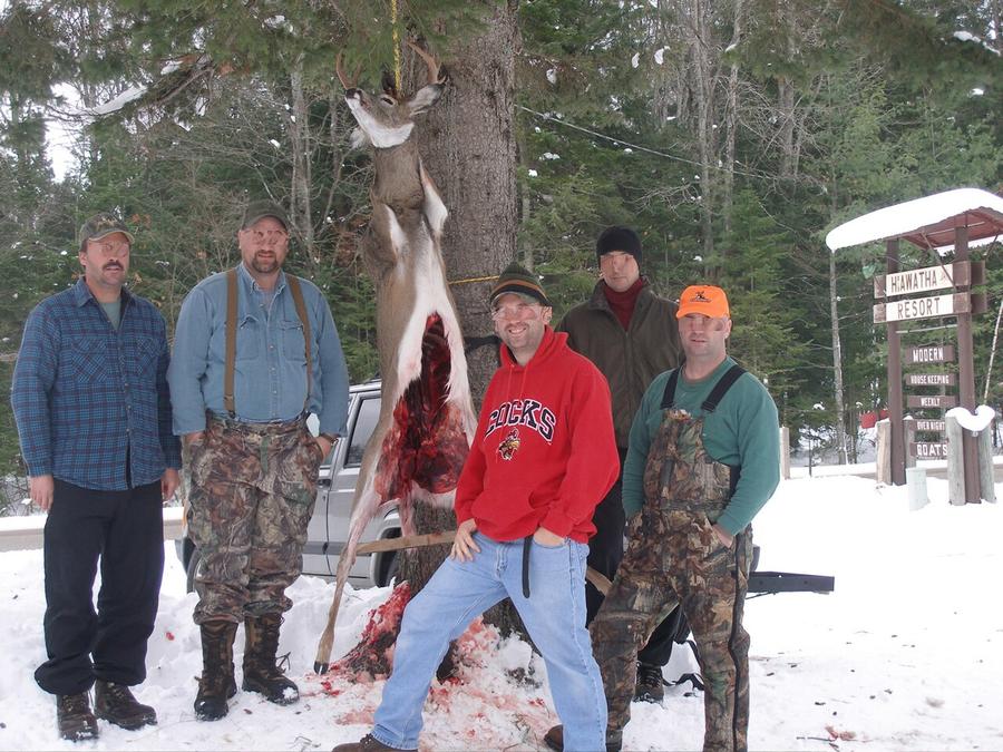Hunters beside a field-dressed deer hung up to cool