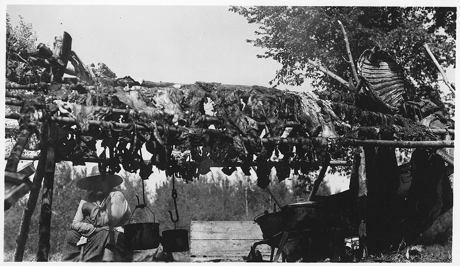 A woman standing beside wooden racks of drying meat