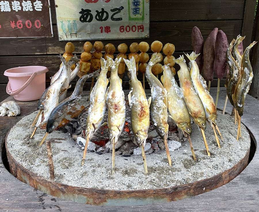 Small fish roasting on sticks pushed into the ground around a fire