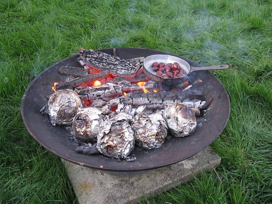 A pan of chestnuts roasting over the embers of an outdoor fire